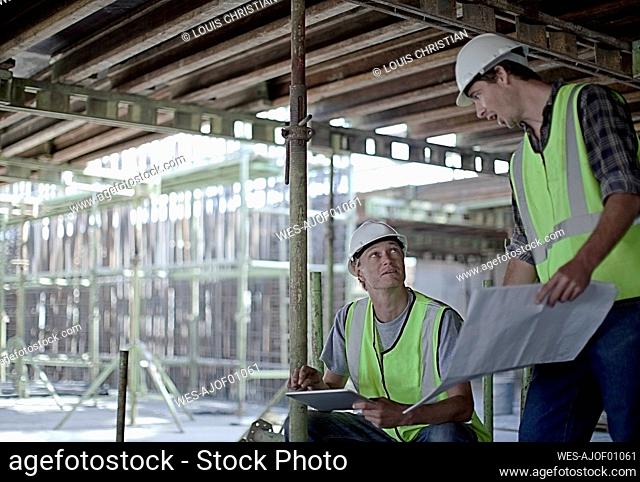 Male construction workers holding digital tablet while planning with coworker at construction site