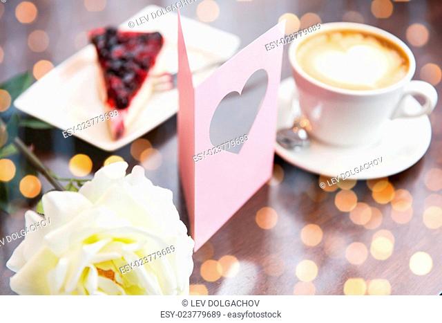holidays, valentines day and love concept - close up of greeting card with heart, flower, cake and coffee over holidays lights