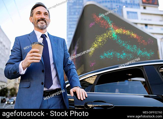 Happy mature businessman with disposable cup by car