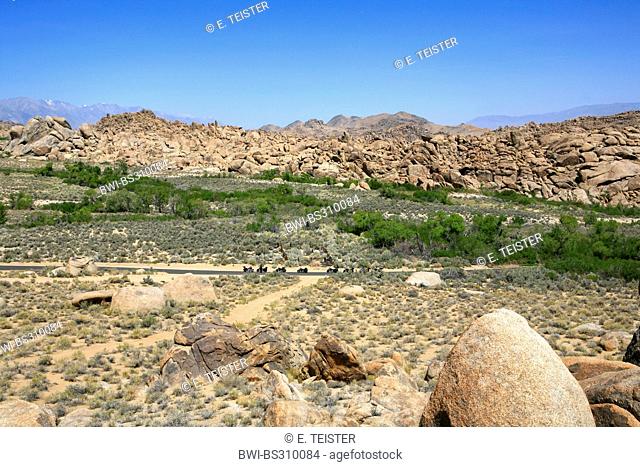 panoramic view over the plains and boulder-like rock formations of the Alabama Hills with some bikers resting at the edge of a country road, USA, California