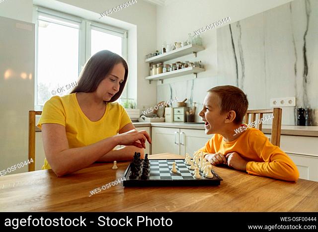 Happy son looking at mother playing chess in kitchen