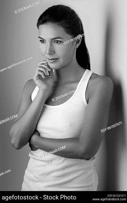 Single beautiful woman in sleeveless blouse with folded arms and hand on chin near wall in black and white