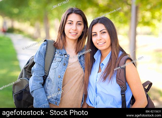 Two beautiful young ethnic twin sisters with backpacks walking outdoors