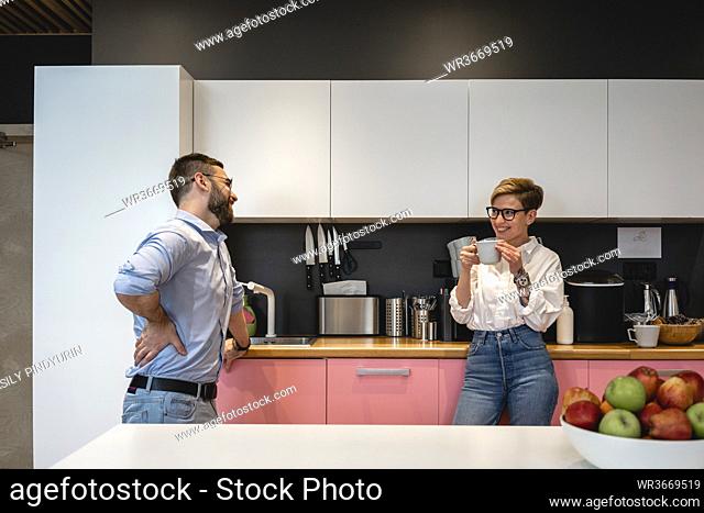Smiling male and female business colleagues talking while enjoying coffee break at cafeteria