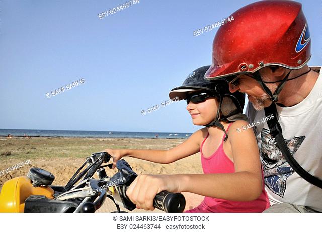 Girl (10) driving an ATV with her dad by seacoast, Djerba Island, Tunisia