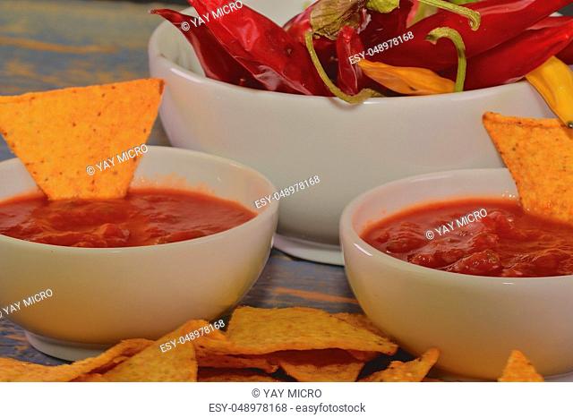 Chili corn-chips with salsa dip and chili peppers on wooden background