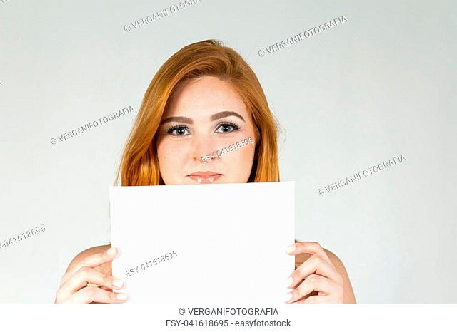 Pretty girl has a faint smile on her lips. She is presenting an advertising content in a blank card. Young white girl with red hair. Isolated
