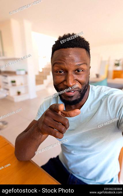 Happy african american man sitting at table and having video call, pointing to camera