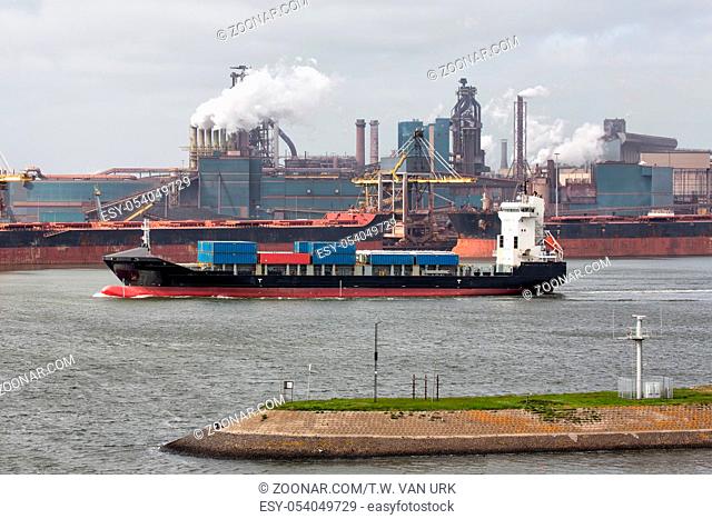 Big steel factory in harbor IJmuiden with cargo carriers and container ship in front, The Netherlands