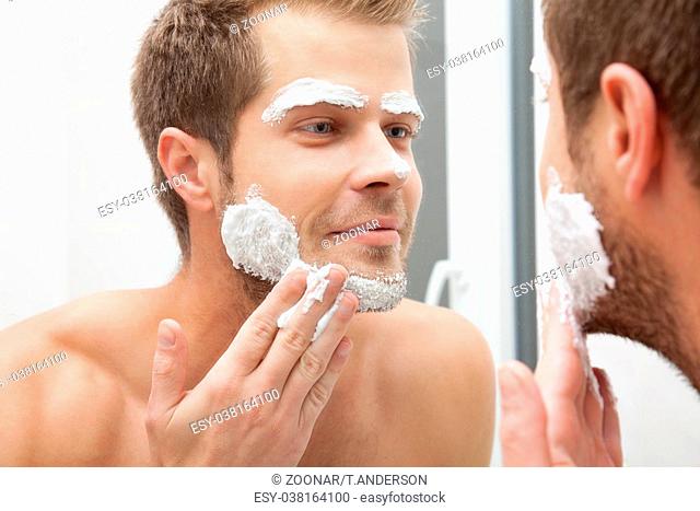 Man looking into the mirror and applying shaving foam