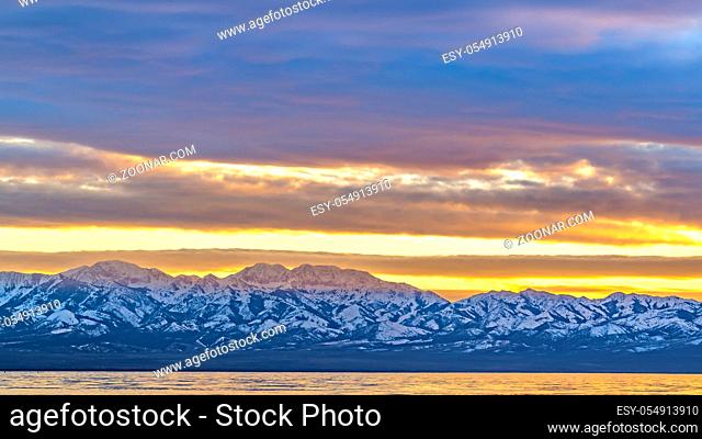 Panorama Panoramic view of a shiny lake and mountain covered with sharp white snow. The cloud filled sky overhead has a golden glow at sunset