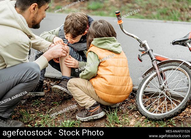 Father comforting son's wound sitting at roadside near bicycle