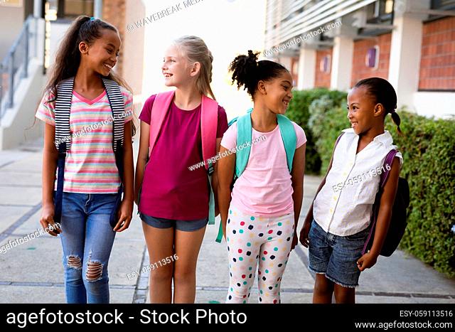 Group of diverse female students with backpacks smiling while looking at each other at school