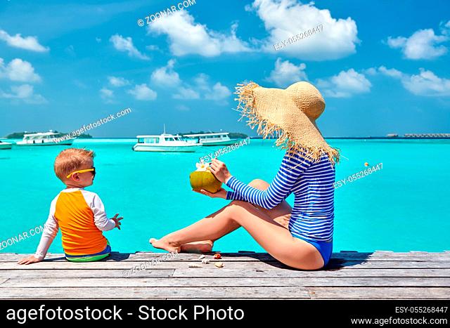 Three year old toddler boy with mother sitting on wooden jetty. Summer family vacation at Maldives