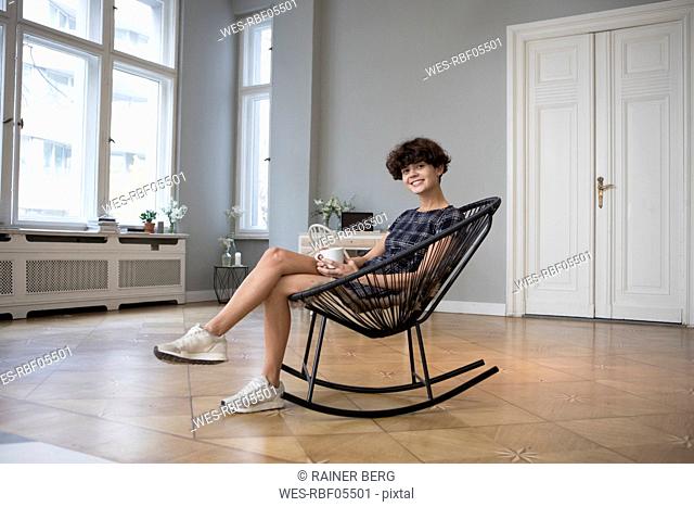 Portrait of smiling young woman sitting on rocking chair at home