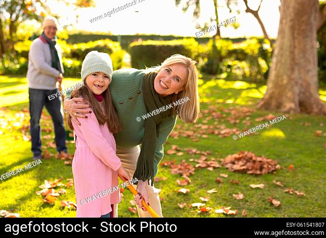 Image of happy caucasian grandmother and granddaughter swiping leaves in garden
