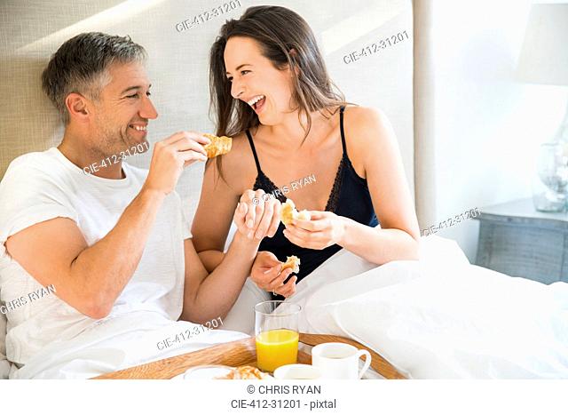 Laughing couple enjoying breakfast in bed