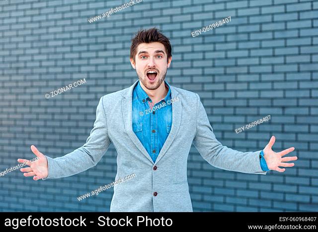 Portrait of amazed handsome bearded man in casual style standing and looking at camera with raised arms and surprised face