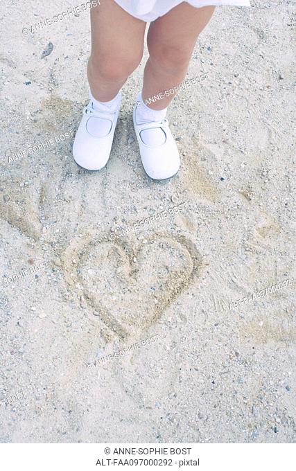 Child standing over heart drawn in sand