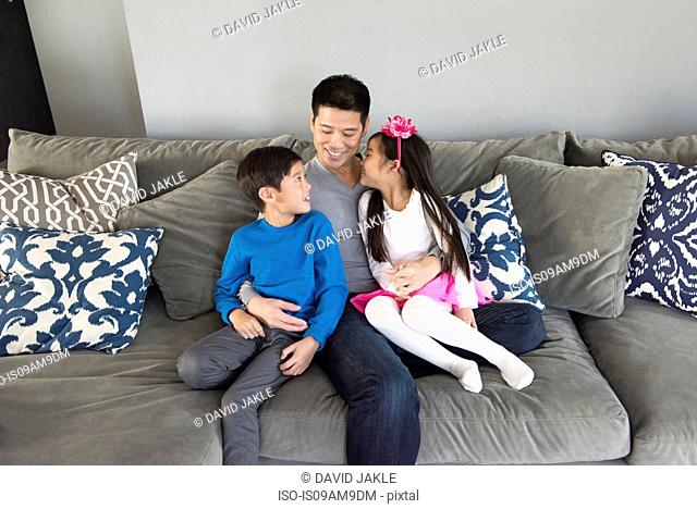 Mature man and two children sitting on living room sofa