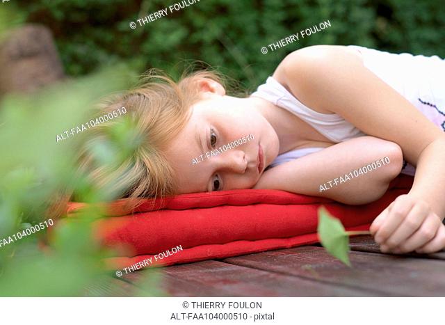 Girl lying on cushion outdoors with leaf in hand