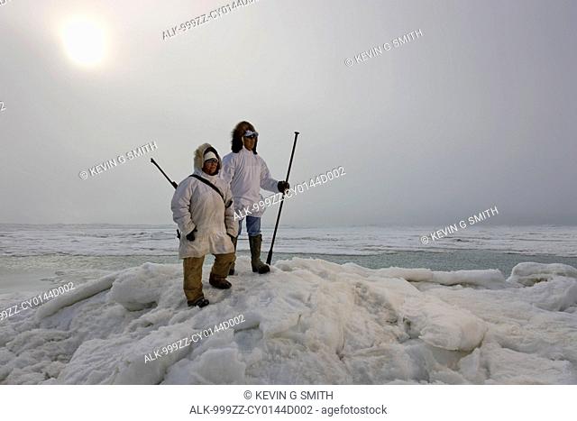 Male and female Inupiaq Eskimo hunters wearing their Eskimo parka's Atigi carry a rifle and walking stick while looking out over the Chukchi Sea, Barrow