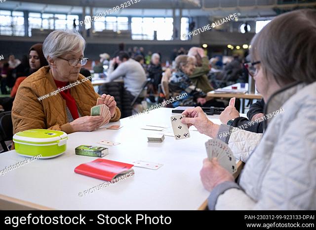 12 March 2023, Hesse, Hanau: Renate (r) and Stanki play the card game Canasta with Michael (hidden) in the August Schärttner Hall