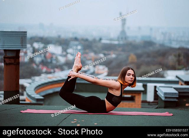 Young woman practicing yoga on the mat on the roof and doing yoga exercises