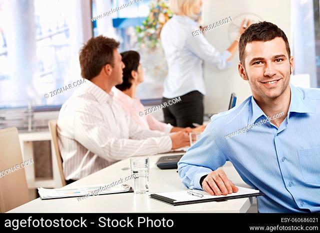 Happy young businessman in business meeting at office, looking at camera smiling