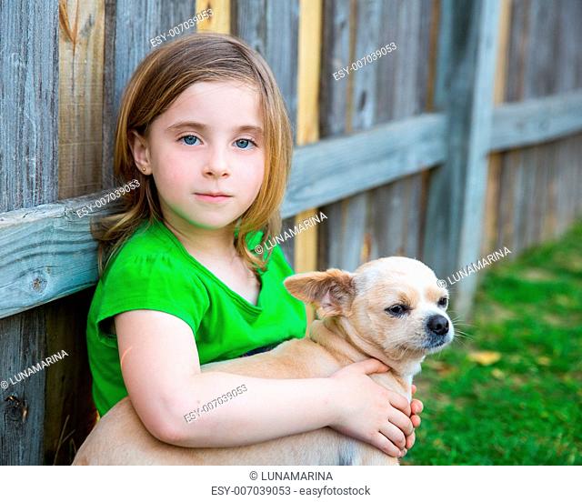 Blond happy girl with her chihuahua doggy portrait on backyard fence