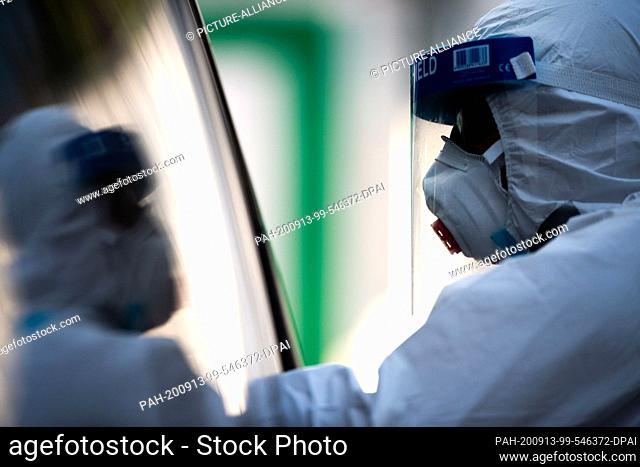 13 September 2020, Bavaria, Garmisch-Partenkirchen: A member of staff uses chopsticks in a test centre to test a family in a car for the coronavirus