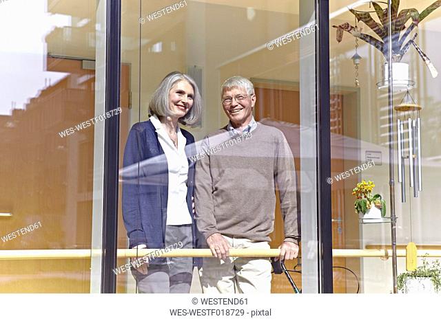 Germany, Cologne, Senior couple looking through window, smiling