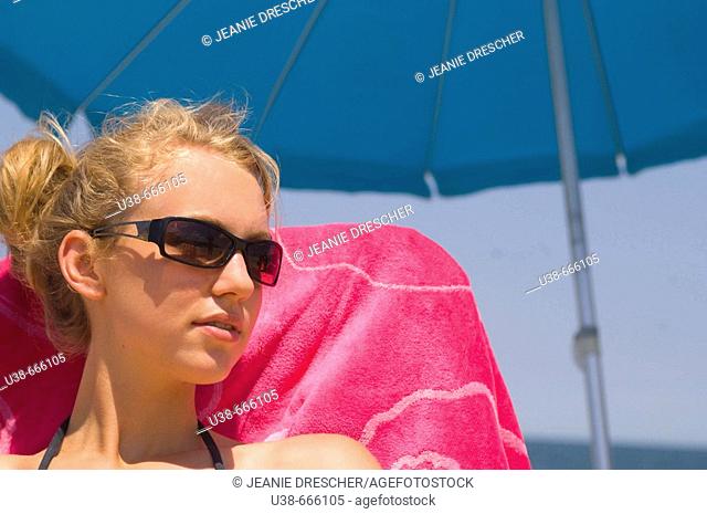Young woman enjoying sitting at the beach under an umbrella. Sandbridge Beach, Virginia Beach, Virginia, USA