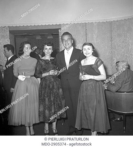Italian actor Rossano Brazzi posing with some fans at the cocktail for the end of the shooting of the film Legend of the Lost. 1957