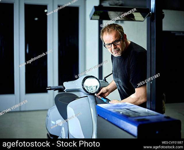 Mechanic adjusting headlight on motor scooter at auto repair shop