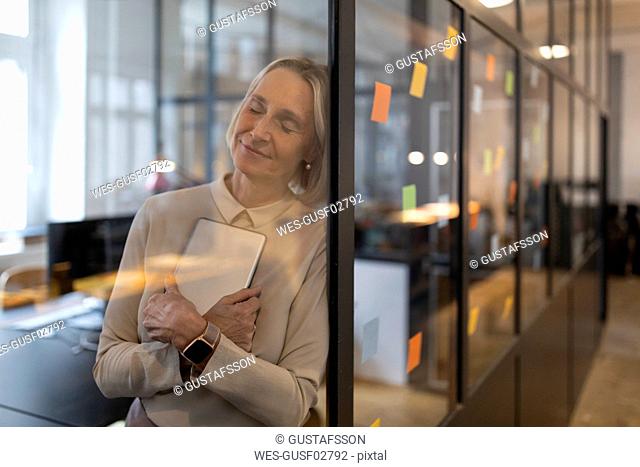 Mature businesswoman with closed eyes leaning against glass pane in office
