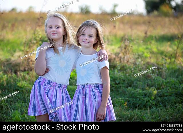 Two little girls friends or sisters stand in a field in summer