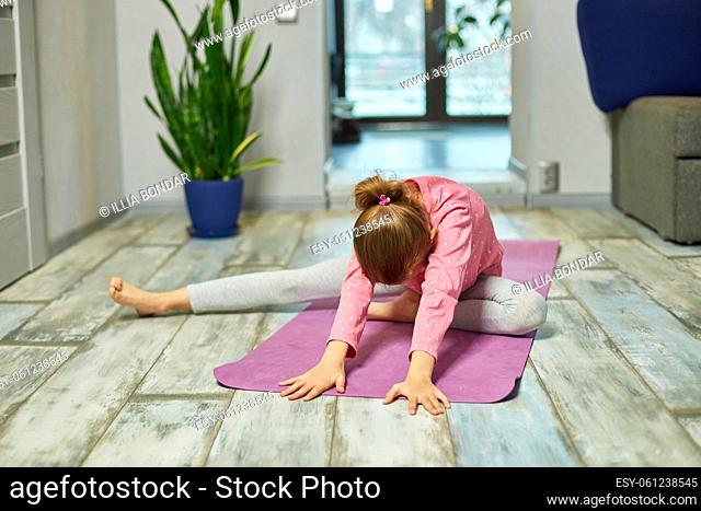 Little girl doing stretching exercises, practicing yoga on fitness mat at  home Stock Photo