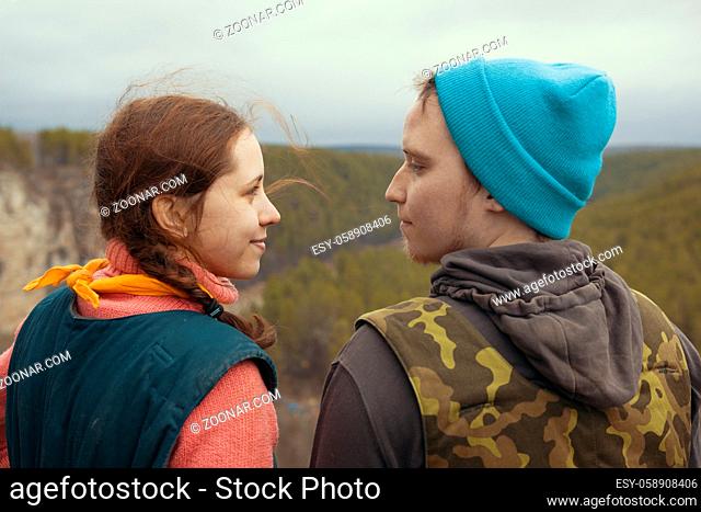 Young couple hikers standing on the edge of a cliff over the mountain river and looking to each other, telephoto shot