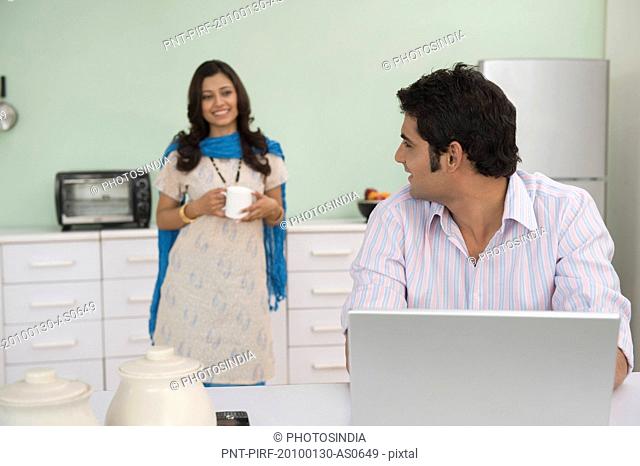 Man working on a laptop with his wife serving coffee