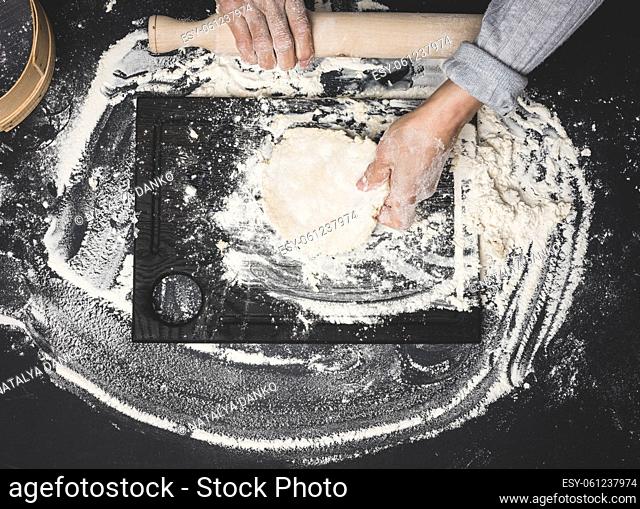 two female hands knead the dough from white wheat flour on a black table, top view