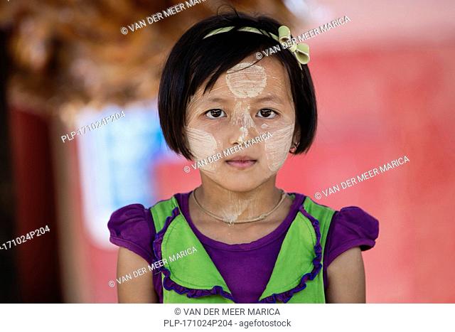 Burmese young girl wearing thanaka on her face, cosmetic yellow powder which gives a cooling sensation and provides protection from sunburn, Myanmar / Burma