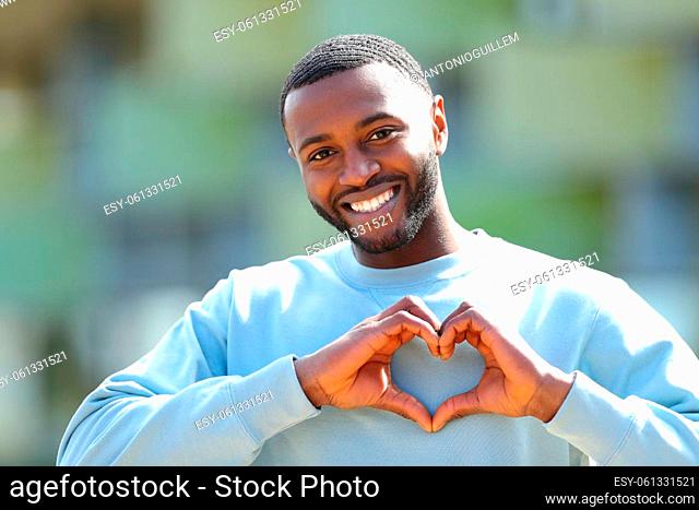Front view portrait of a happy man with black skin doing heart shape outdoors