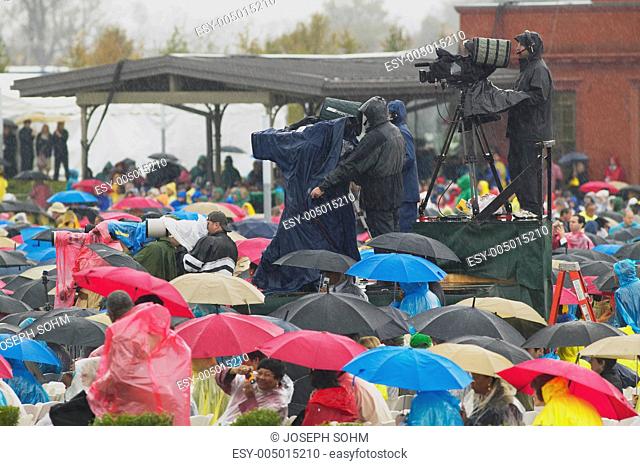 Guests hold umbrellas in the rain as cameramen record the official opening ceremony of the Clinton Presidential Library November 18, 2004 in Little Rock, AK