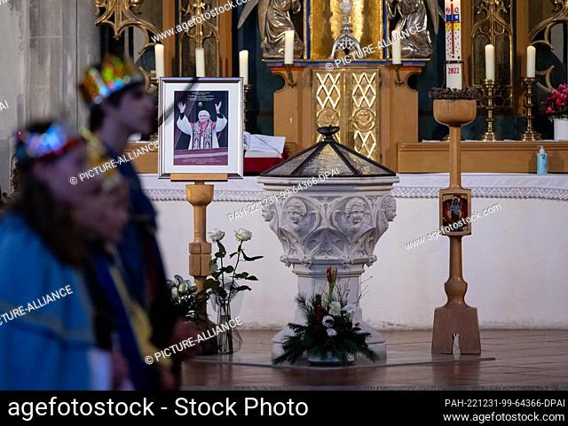 31 December 2022, Bavaria, Marktl: Carolers attend a service at St. Oswald Church in front of a picture of Pope Emeritus Benedict XVI