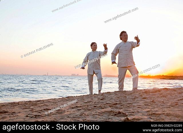 Two older people practicing Taijiquan on the beach at sunset, China