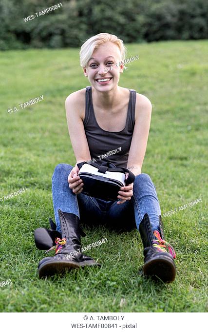 Portrait of amazed young woman sitting on meadow with Virtual Reality Glasses