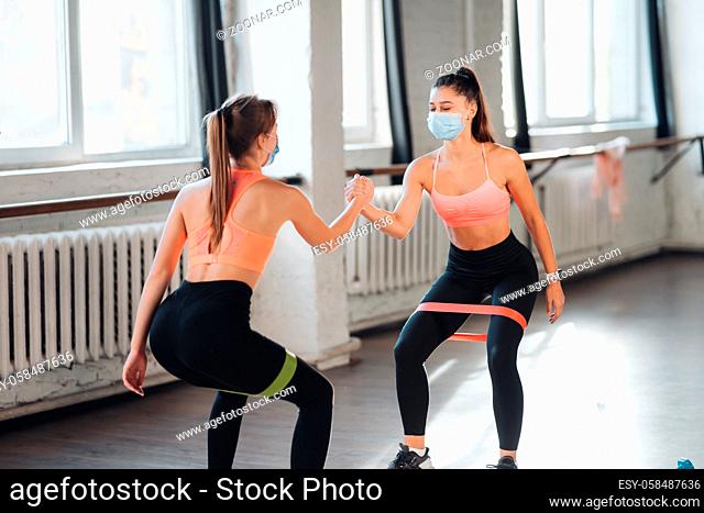 Young women doing push up exercise in room during morning. Slim girls wearing masks to protect covid-19 disease pandemic and social distancing