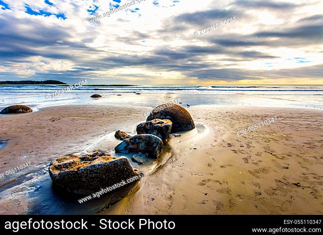 The popular tourist attraction. New Zealand. Sandy beach on the Pacific Ocean. The picturesque group of huge round stone boulders Moeraki and their remains