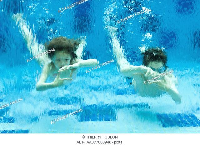 Brother and sister swimming underwater in swimming pool, hands forming finger frames